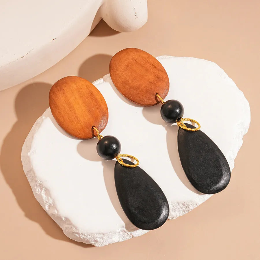 A pair of brown and black wooden ellipse earrings with a retro design on a plain background.