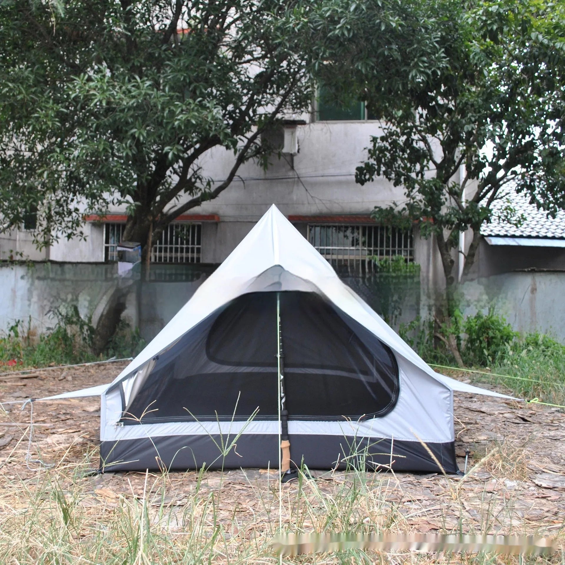 Brown A-line tent pitched with hiking poles, showing guy lines and aluminium ground nails.