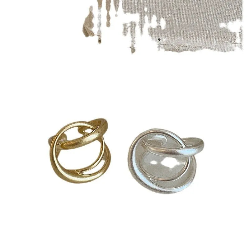 Geometric open ring for women with a 3D interlaced design in matte metal, shown in gold and silver finishes.