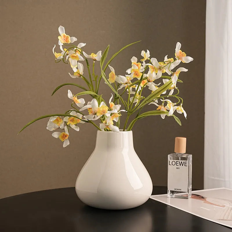 Black ceramic round belly vase with white orchid flowers on wooden shelf