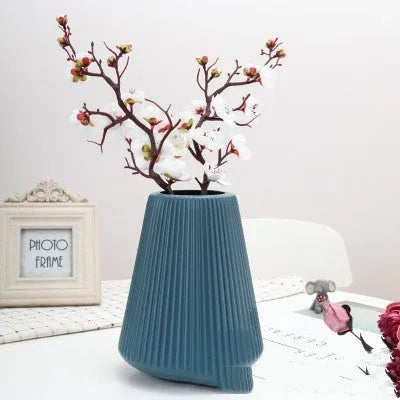 A simple white melamine plastic decorative flower vase on a wooden tabletop.
