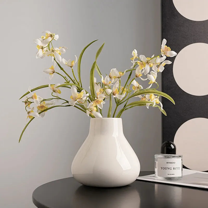 Black ceramic round belly vase with white orchid flowers on wooden shelf