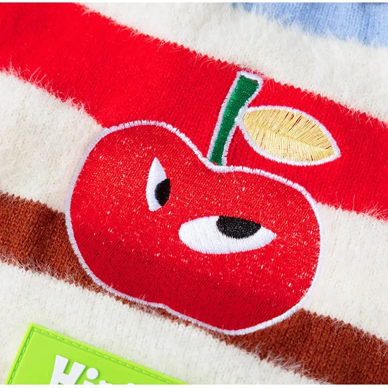 Corgi dog wearing a rainbow apple striped knitted pullover sweater in brown, standing on grass