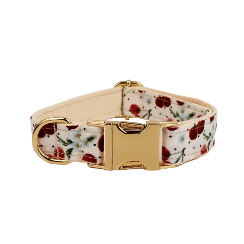 Red cherry printed cloth dog collar set with light gold buckle, matching leash, bow, vest, and bag.