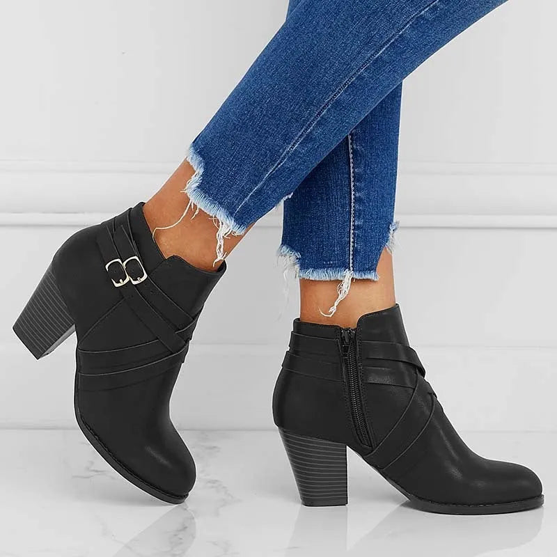 Plus size black short ankle boot with a 7cm heel, side zip, and buckle detail on a grey background.