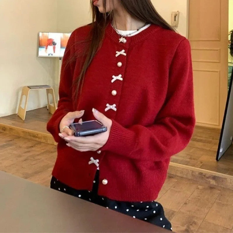 Women's light pink cardigan sweater with a black bow detail and pearl buttons on a hanger.