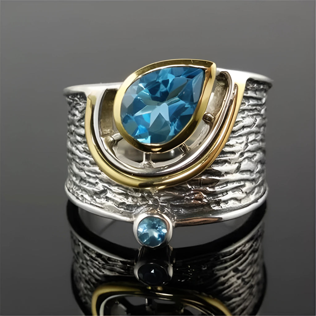 Blue zircon drop-shaped ring with Chinese style rhinestone inlay, shown on a finger.