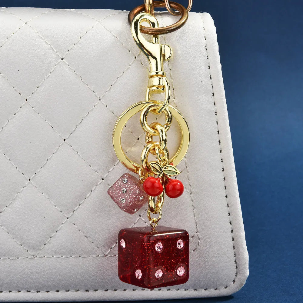 Close-up of a cherry red and white metal dice keychain pendant with a square pattern on a vintage-style suitcase charm.