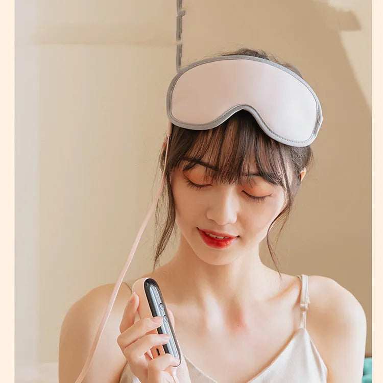Pink portable eye spa massage goggles with USB cable on a grey background.