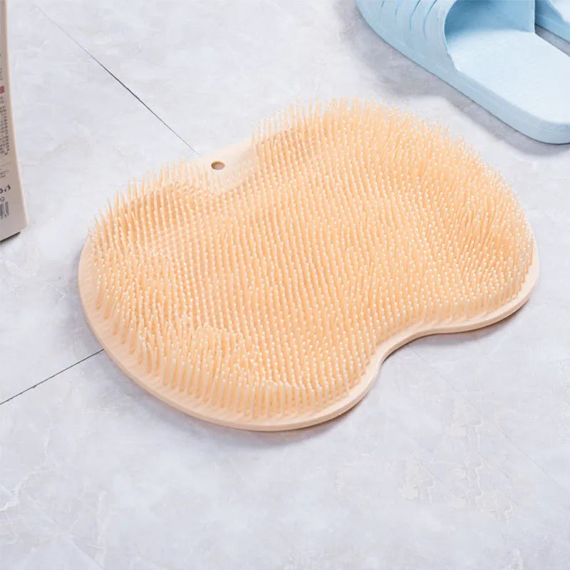 Orange non-slip massage bath brush with suction cups and soft silicone bristles on a bathroom floor.