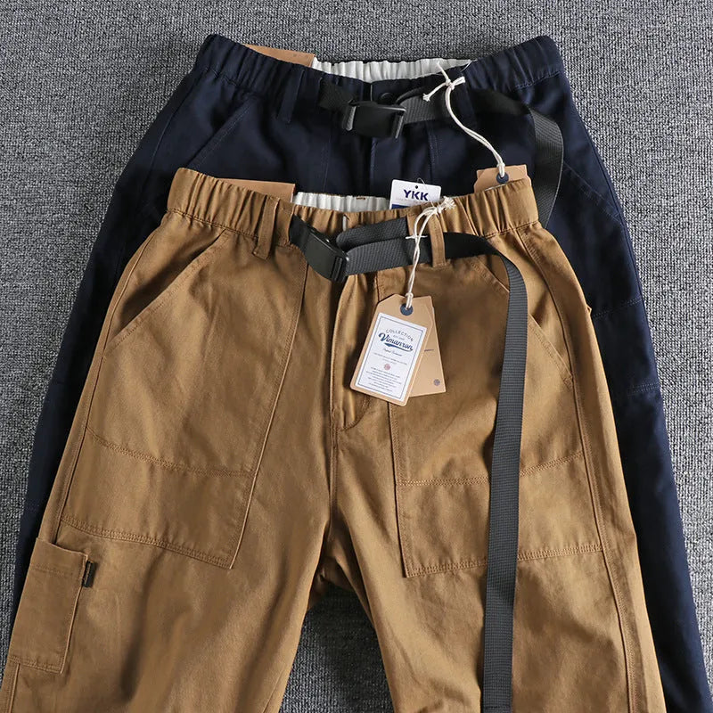 A pair of men's khaki cotton work trousers with a mid waist and zip fly on a plain background.