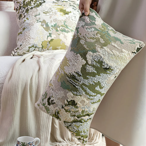 Antique green square pillow with abstract spring flowers pattern on a grey sofa.