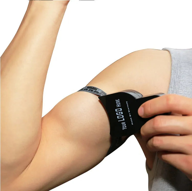 Black body fat caliper skin fold measuring instrument with two coiled measuring tapes on a grey background.