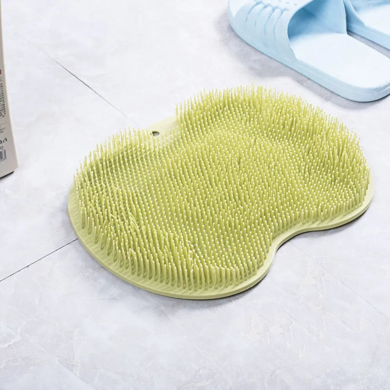 Orange non-slip massage bath brush with suction cups and soft silicone bristles on a bathroom floor.