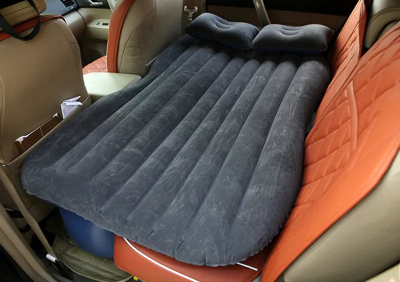 Black inflatable car bed with flocked surface and pillows set up in a car's back seats