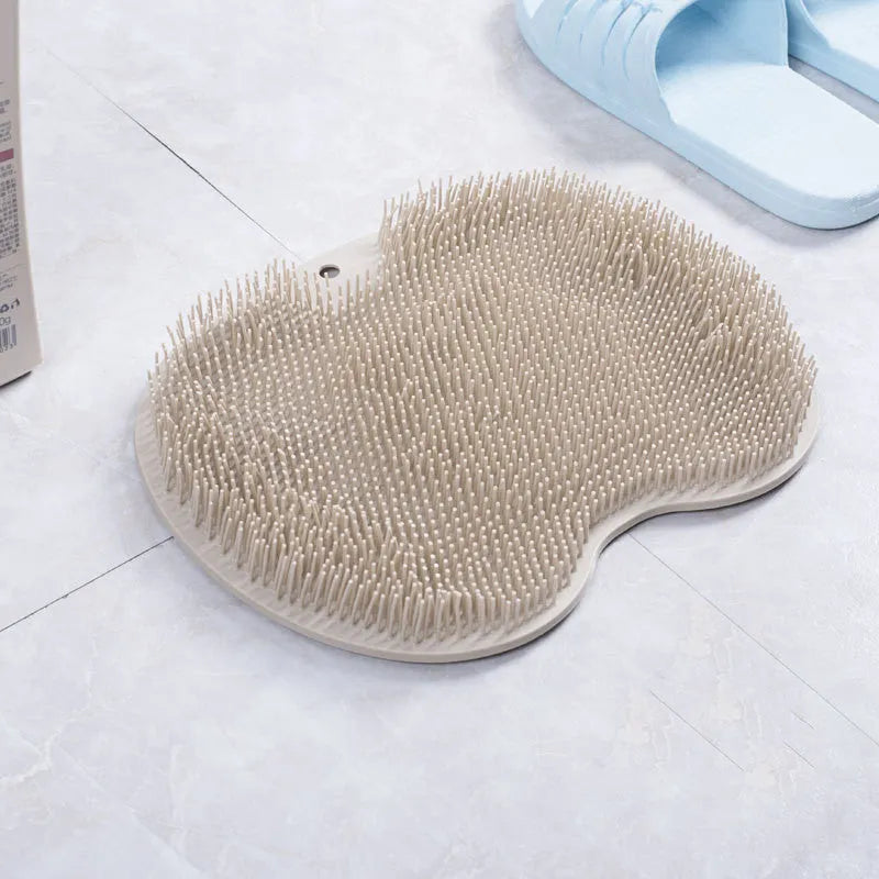 Orange non-slip massage bath brush with suction cups and soft silicone bristles on a bathroom floor.