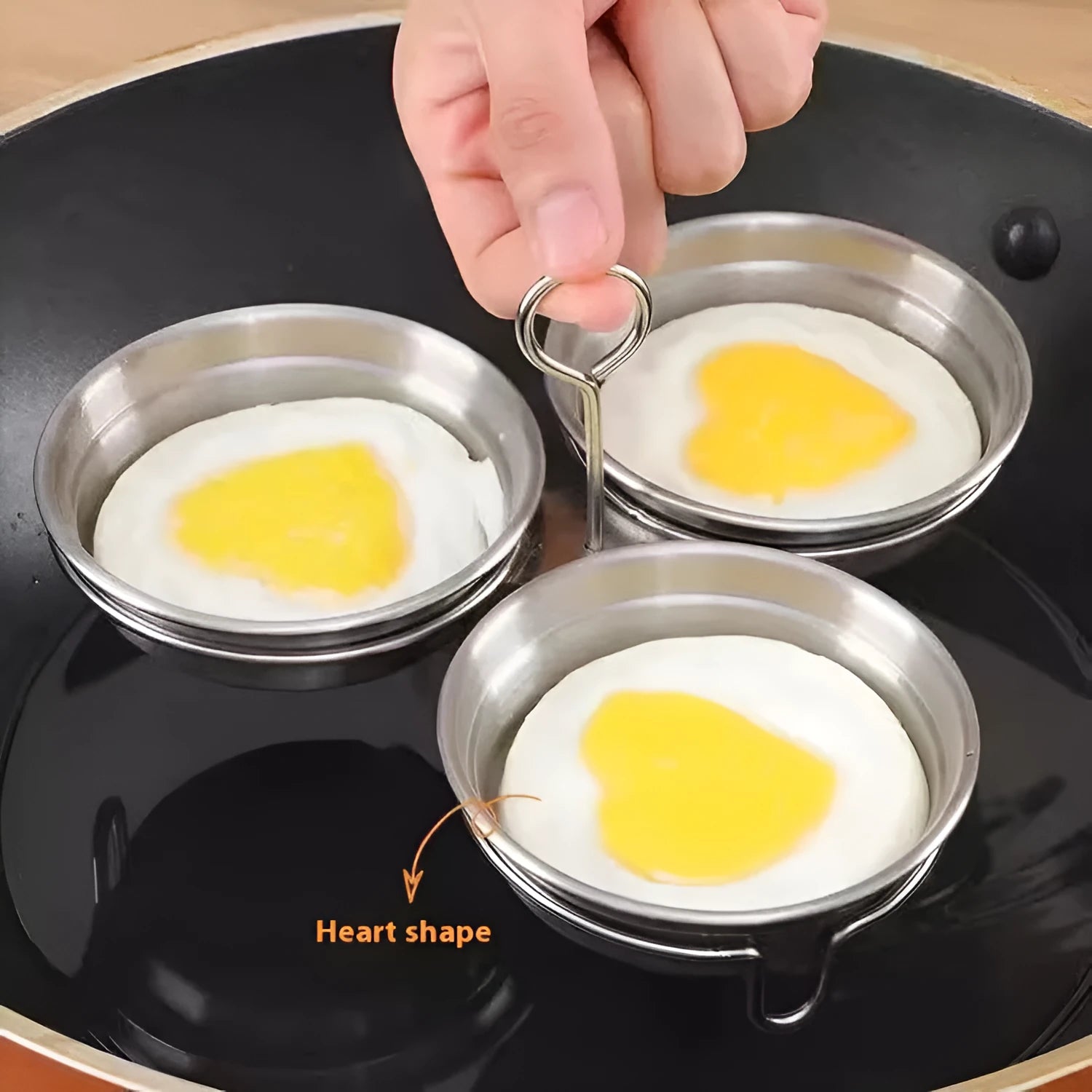 A small stainless steel egg steamer in a heart shape next to a round version, for cooking eggs on a hob.