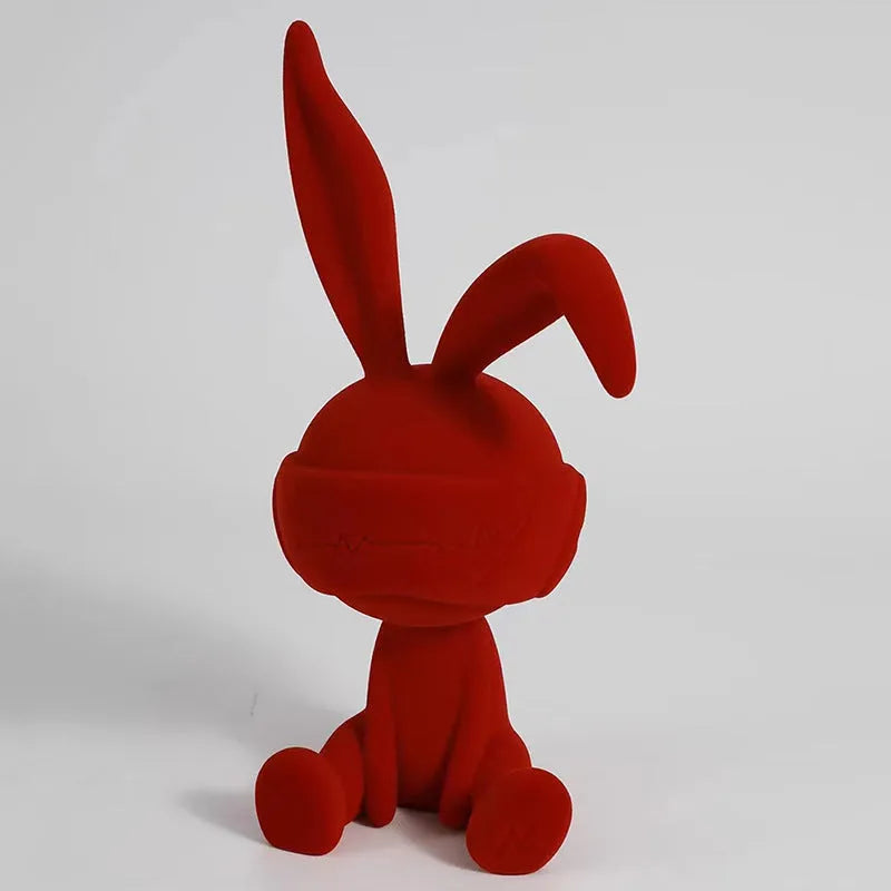 Green resin rabbit table ornament with a suede blindfold on a wooden shelf.