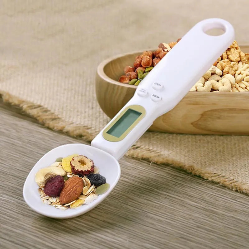 White digital kitchen spoon scale with LCD display showing 0.0g on a wooden table