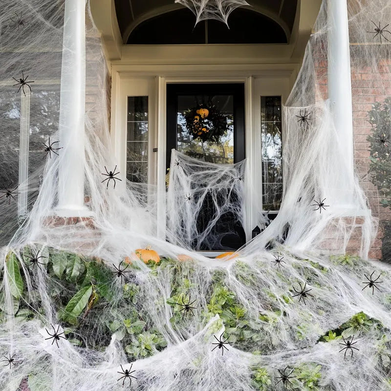 White cotton spider web Halloween decoration with plastic spiders draped over a surface.