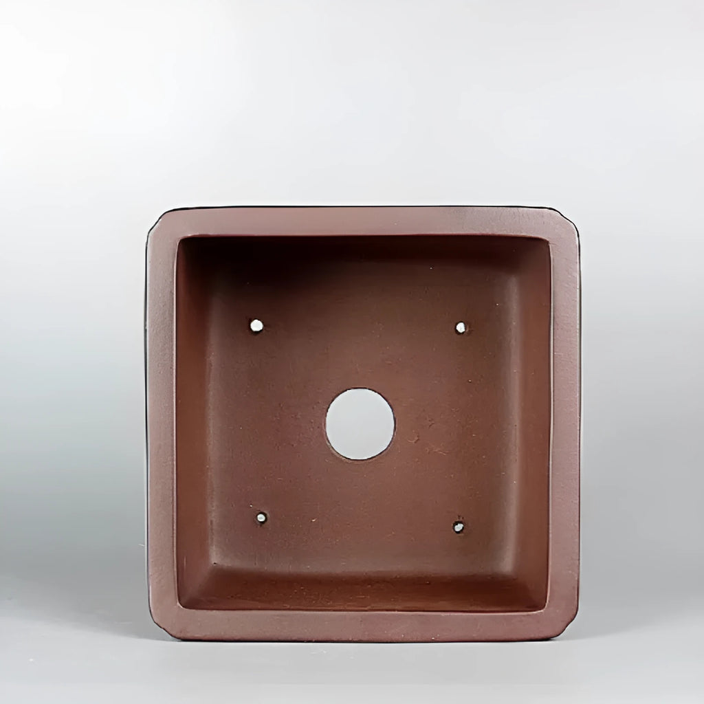 Handmade brown antique-style purple clay flower pot for houseplants on a desk.