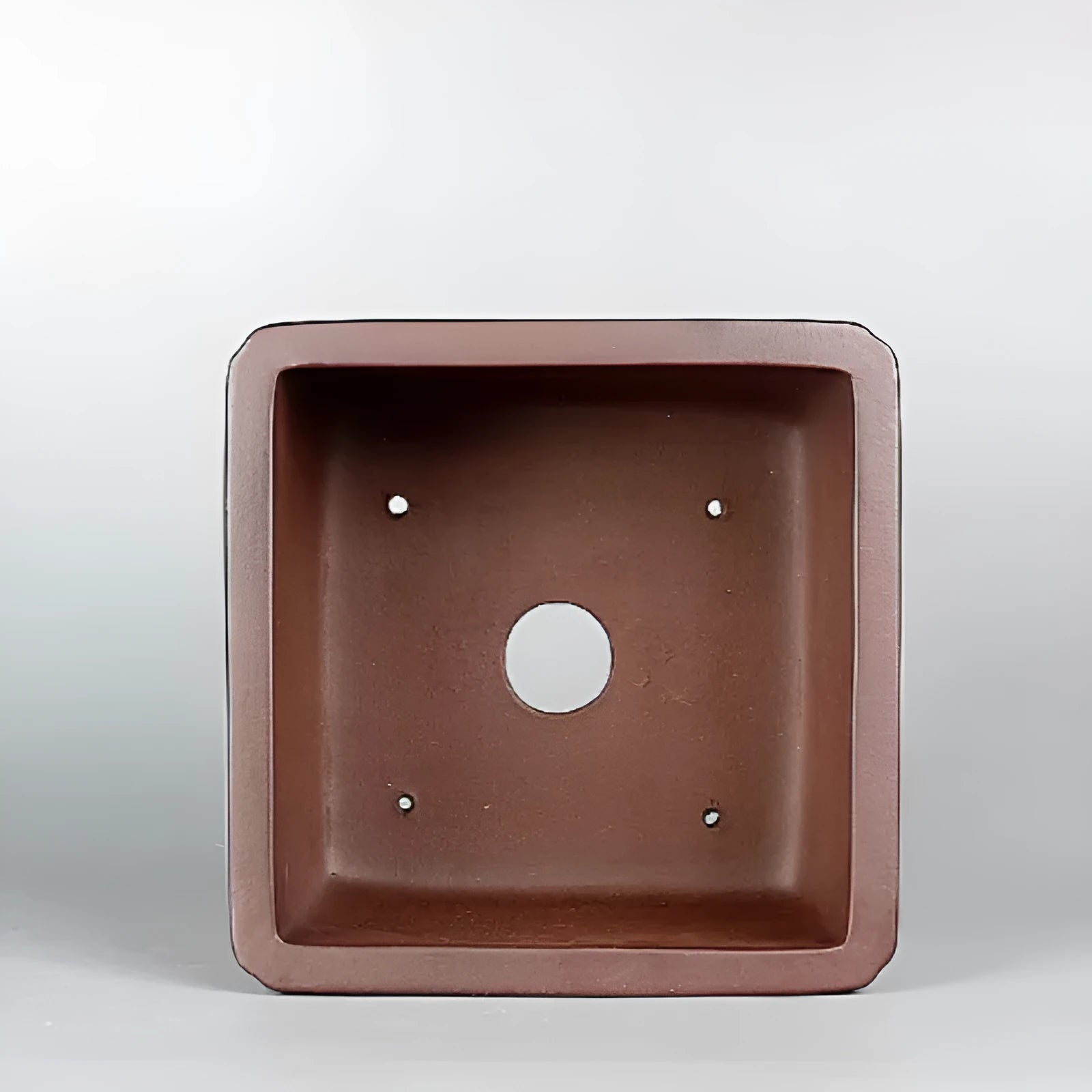 Handmade brown antique-style purple clay flower pot for houseplants on a desk.