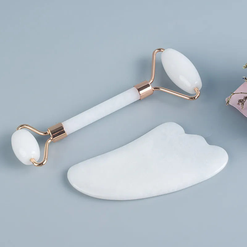 White jade double-headed facial roller and gua sha board set on a flat surface.