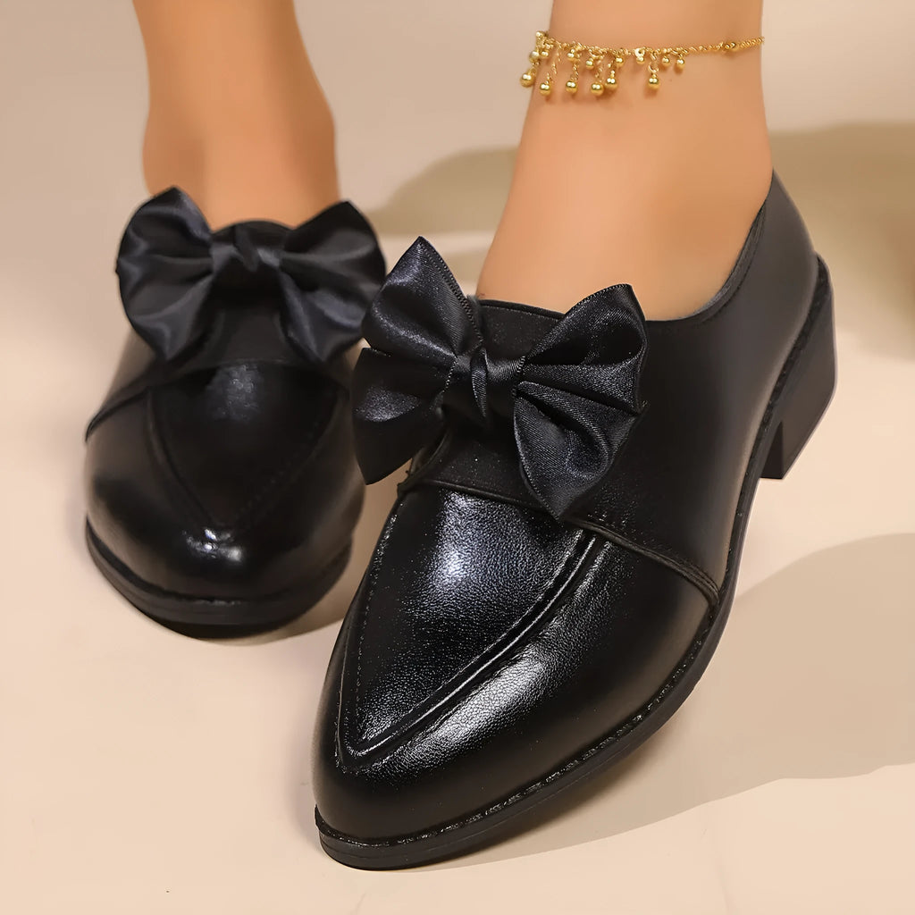 Women's classic black slip-on flat shoes with a large decorative bow on the toe.