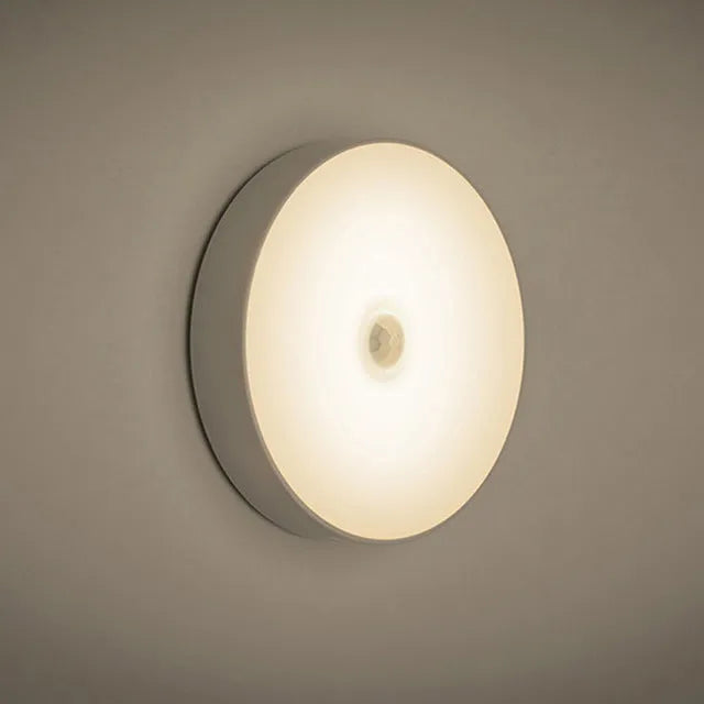 Small circular white motion sensing LED night light with USB charging cable and adhesive tape.