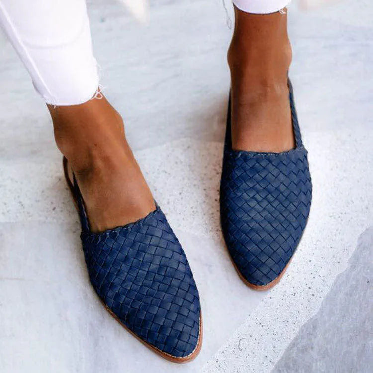 A pair of black baotou flat sandals with a buckle fastening and pointed toe on a plain background.