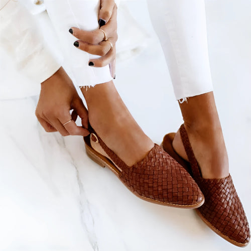 A pair of black baotou flat sandals with a buckle fastening and pointed toe on a plain background.