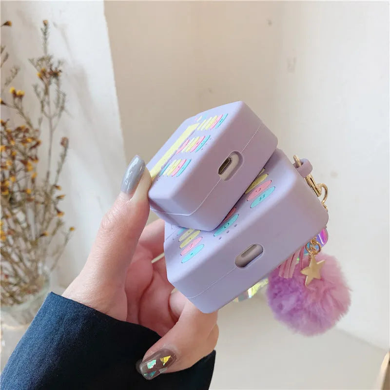 Purple silicone clamshell case for Apple AirPods with a small fur ball pendant attached.