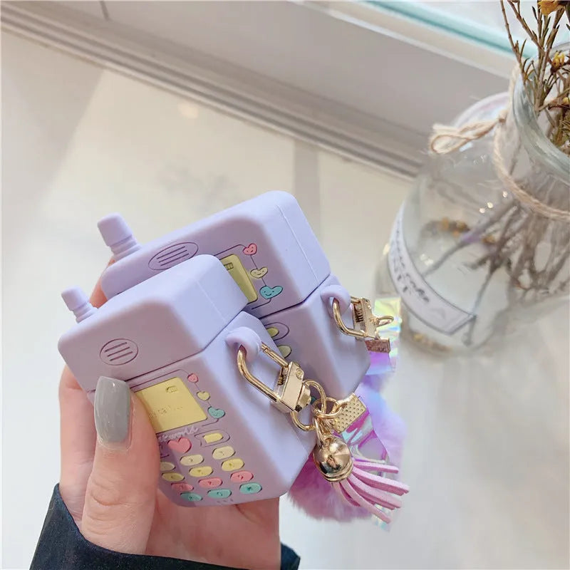 Purple silicone clamshell case for Apple AirPods with a small fur ball pendant attached.
