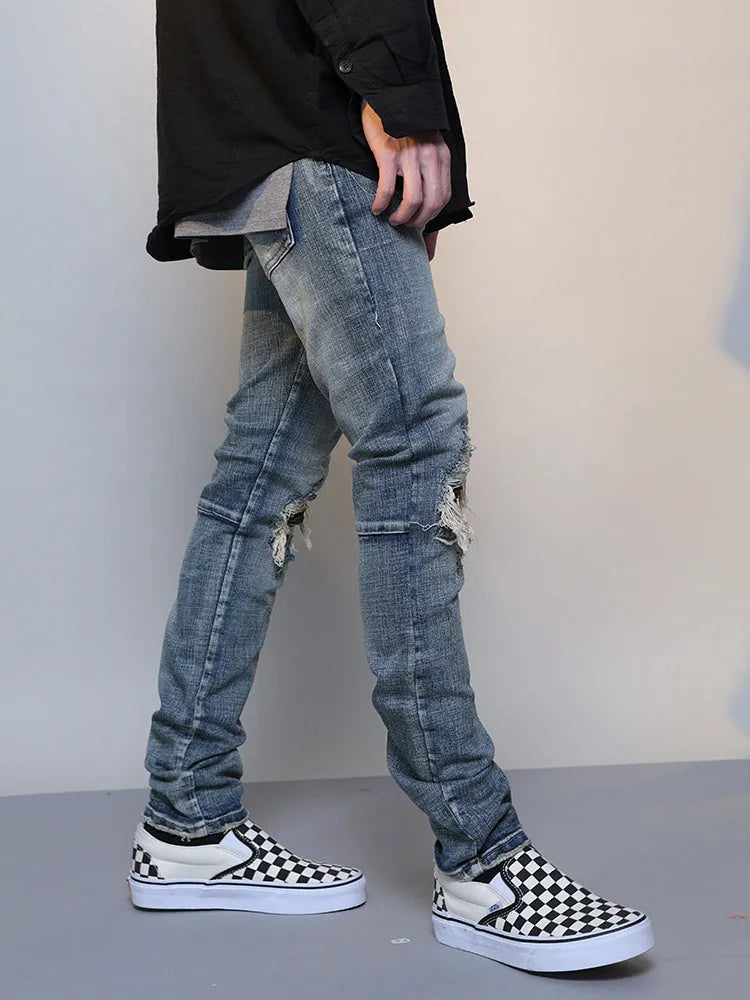 Mens ripped washed blue cotton denim jeans with middle-waisted zip fly, side view on model