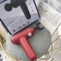 Black fascia gun muscle massager with USB charging port on a grey background.
