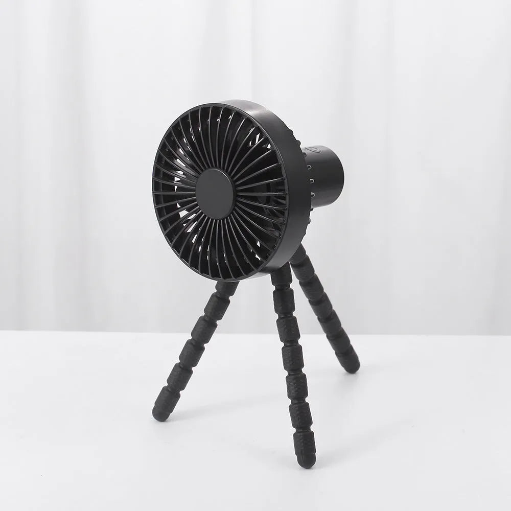 Small adjustable tripod desktop fan with bending head, shown in black on a desk.