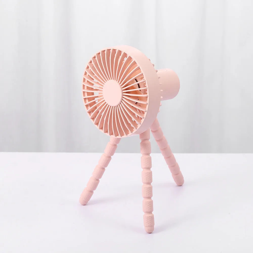 Small adjustable tripod desktop fan with bending head, shown in black on a desk.