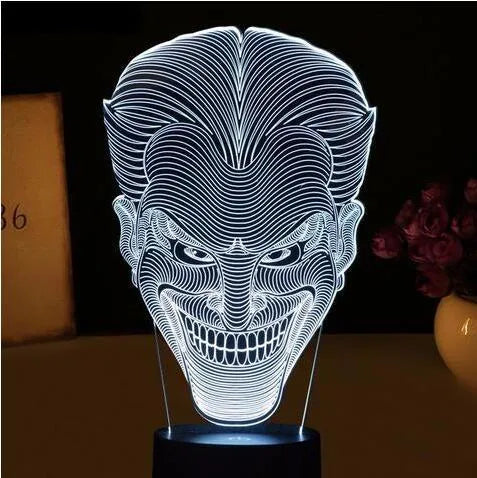 A 3D LED table lamp showing multiple colour lights, sitting on a square base with a USB cable and remote control.