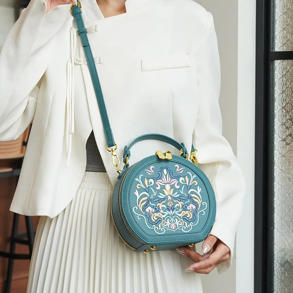 National style round crossbody bag in khaki PU leather with embroidery and sewing line details, shown on a plain background