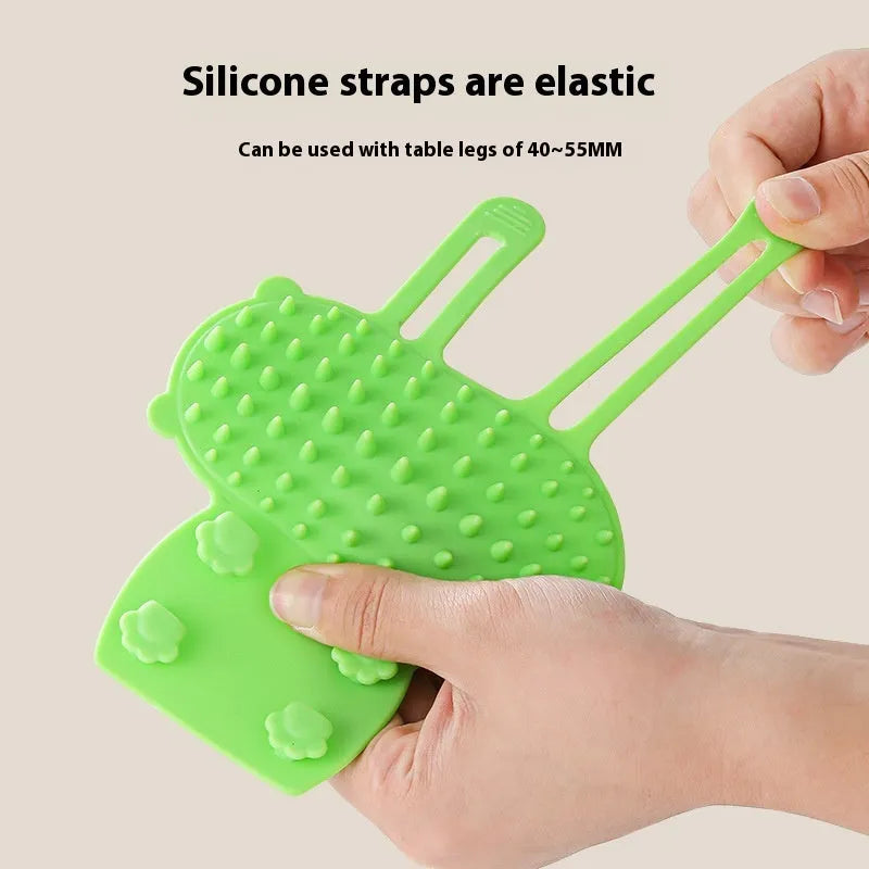 Silicone cat grooming massage comb with adjustable strap mounted on a table leg.
