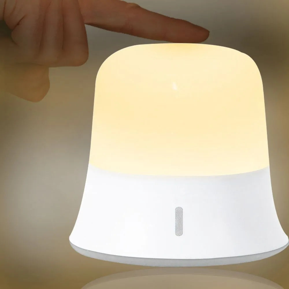 White bedside night light with touch controls for dimming and changing RGB colours on a table.