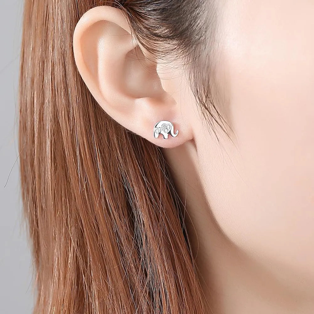 Small geometric silver stud earrings with gold or silvery finish on a grey background.