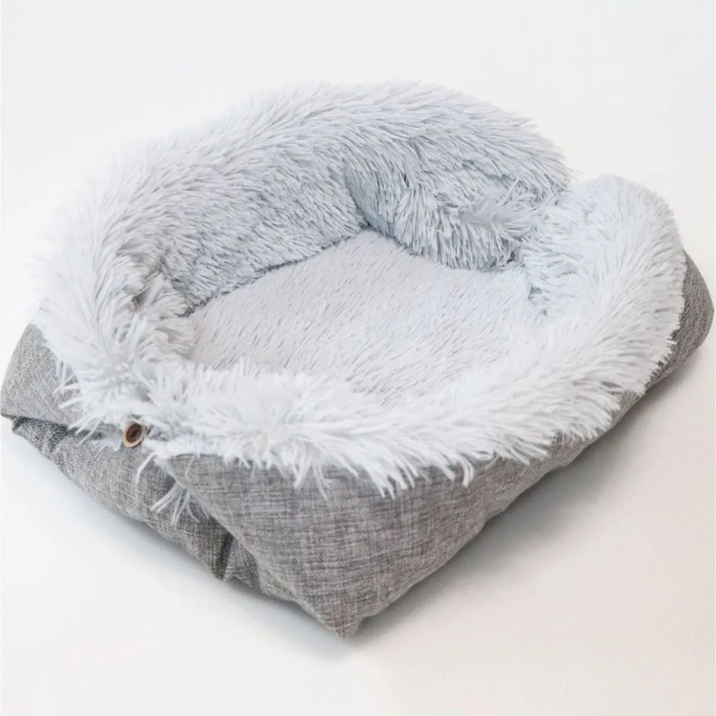 Grey fluffy pet sleeping pad for cats and dogs on a sofa, showing non-slip black bottom.