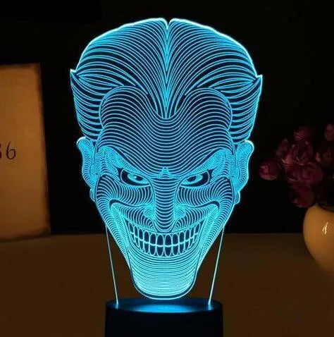 A 3D LED table lamp showing multiple colour lights, sitting on a square base with a USB cable and remote control.