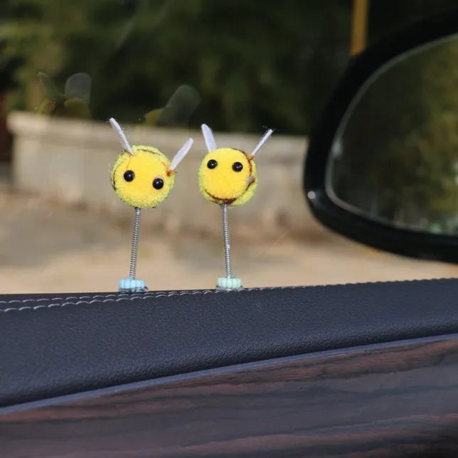 Small yellow and black fur ball bee car decoration on a plastic surface.