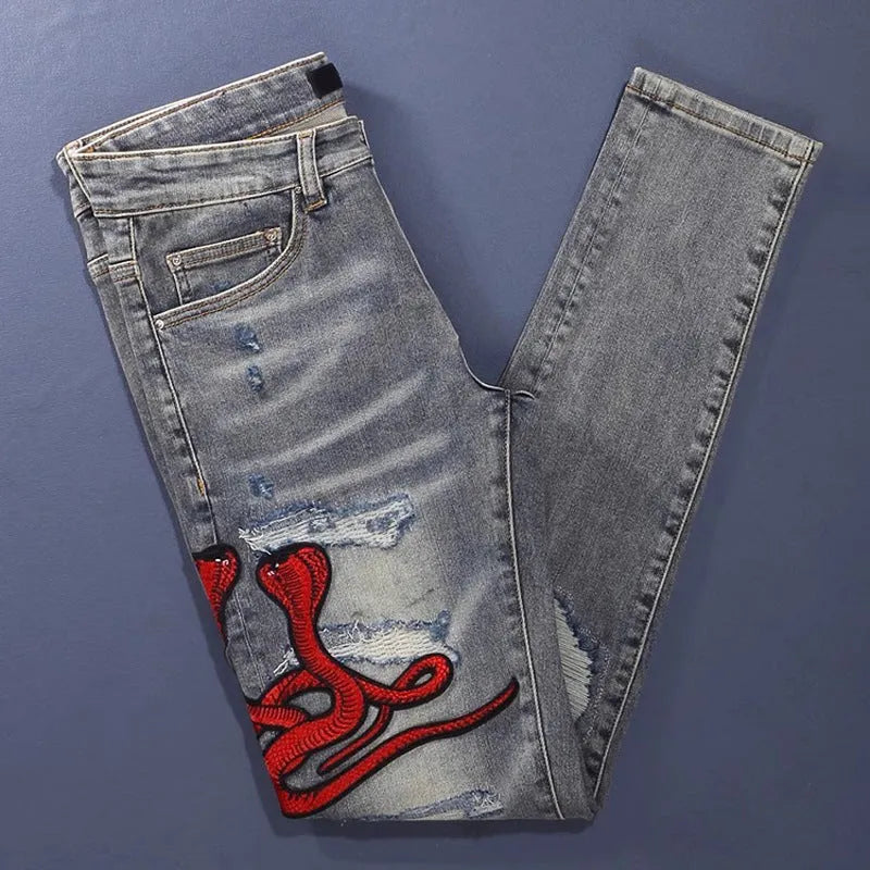Slim-fit light blue jeans with a worn wash, knee holes, patch details, and embroidered branding on the leg.