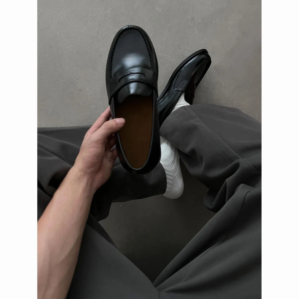 Men's black British-style slip-on leather loafers with stitched seams and vulcanised rubber sole on a plain background