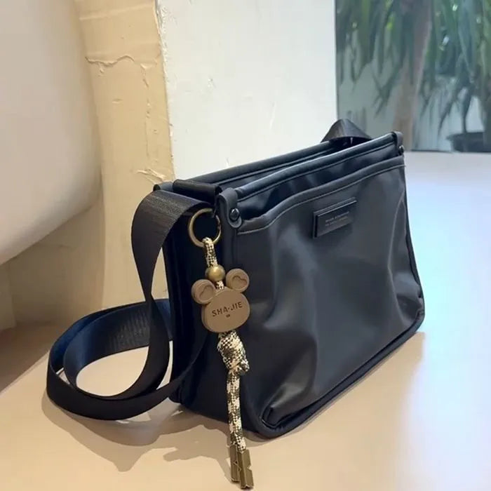 A small square crossbody bag in a cool retro style, made from textured Oxford cloth, shown on a person for scale.
