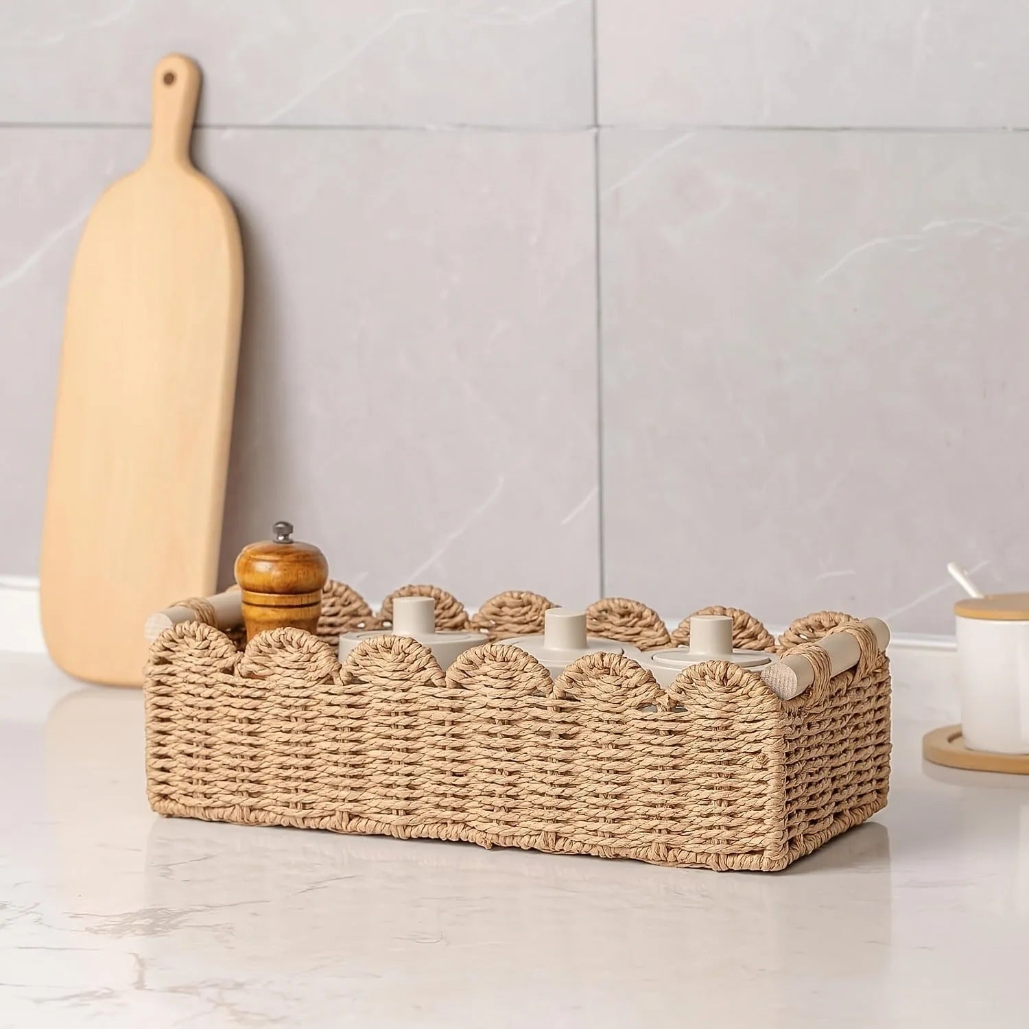 Woven paper storage basket in khaki colour on a desktop holding remote controls and pens.
