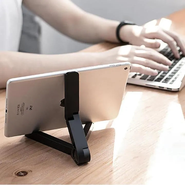 Black foldable tablet stand holding a smartphone in landscape mode on a desk, showing its compact folded size.